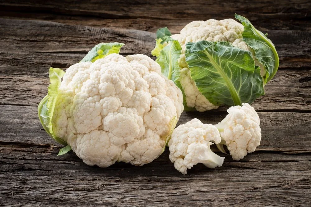 Cauliflower heads and florets on a wooden surface.
